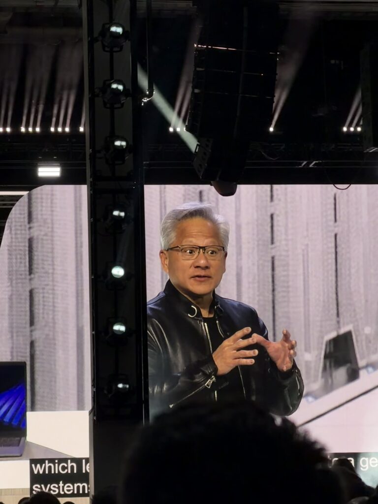 Jensen Huang presenting on stage at Dell Technologies World, shown on a large screen with stage lighting and audience in foreground.